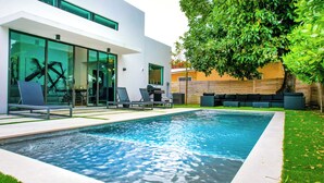 A modern outdoor pool area with a glass-enclosed patio, lounge chairs, and a barbecue grill. - Noir Luxury Home, Design District w/ Pool, Billiard (Miami)