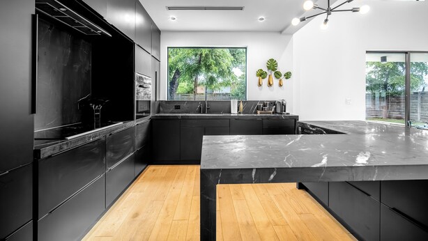 A modern kitchen with dark cabinetry, a marble countertop, and a large window with a view of greenery. - Noir Luxury Home, Design District w/ Pool, Billiard (Miami)