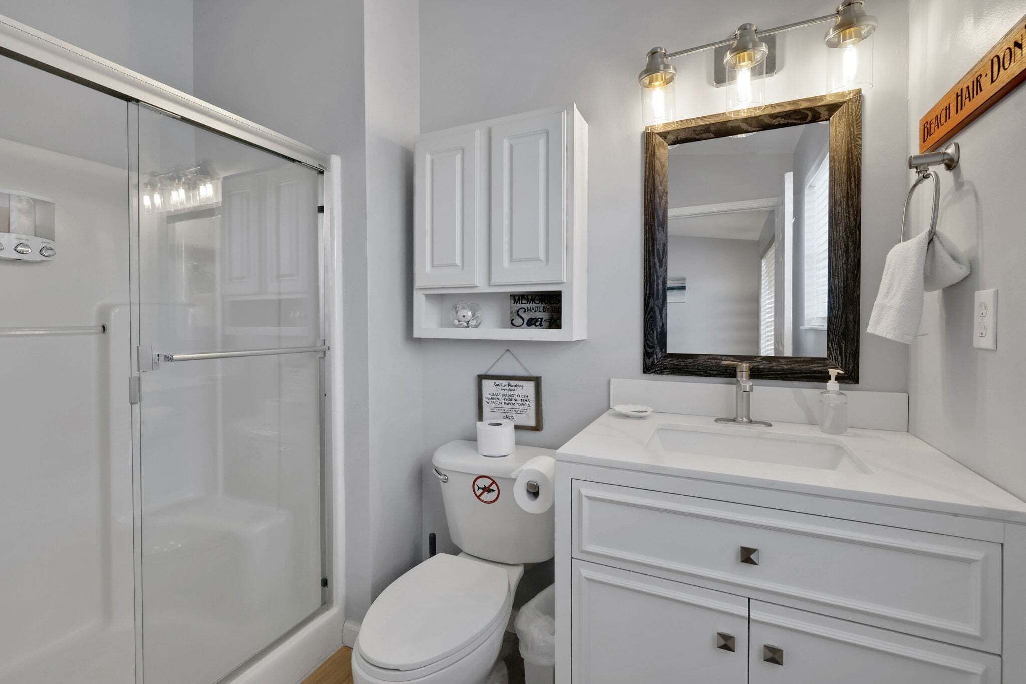 A bathroom with a glass shower enclosure, a toilet with a no-smoking sign, a vanity with a mirror, and a towel rack.