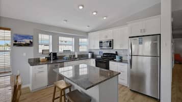 A modern kitchen with white cabinets, a stainless steel refrigerator, a microwave, and a granite countertop island with stools.