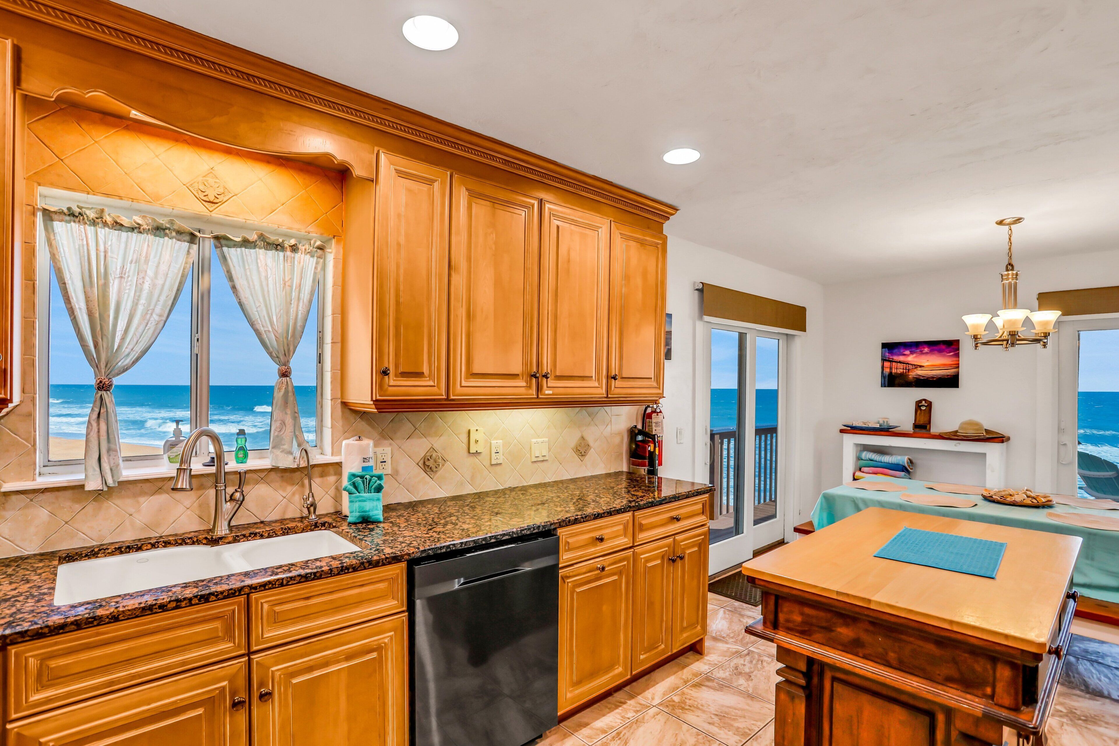 A kitchen with wooden cabinets, a granite countertop, a dishwasher, and a view of the ocean.