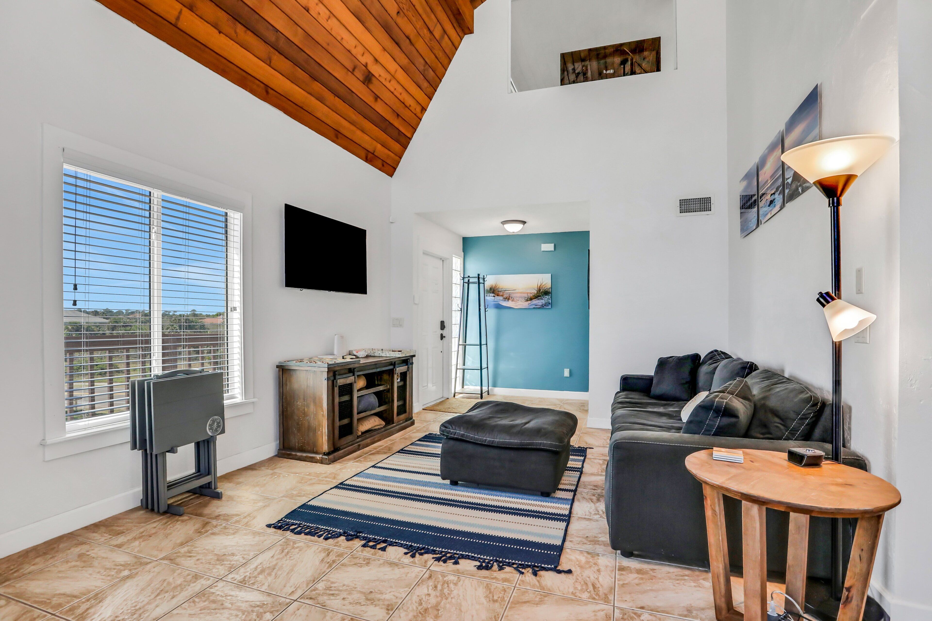 A living room with a TV, a couch, a wooden table, and a blue accent wall.