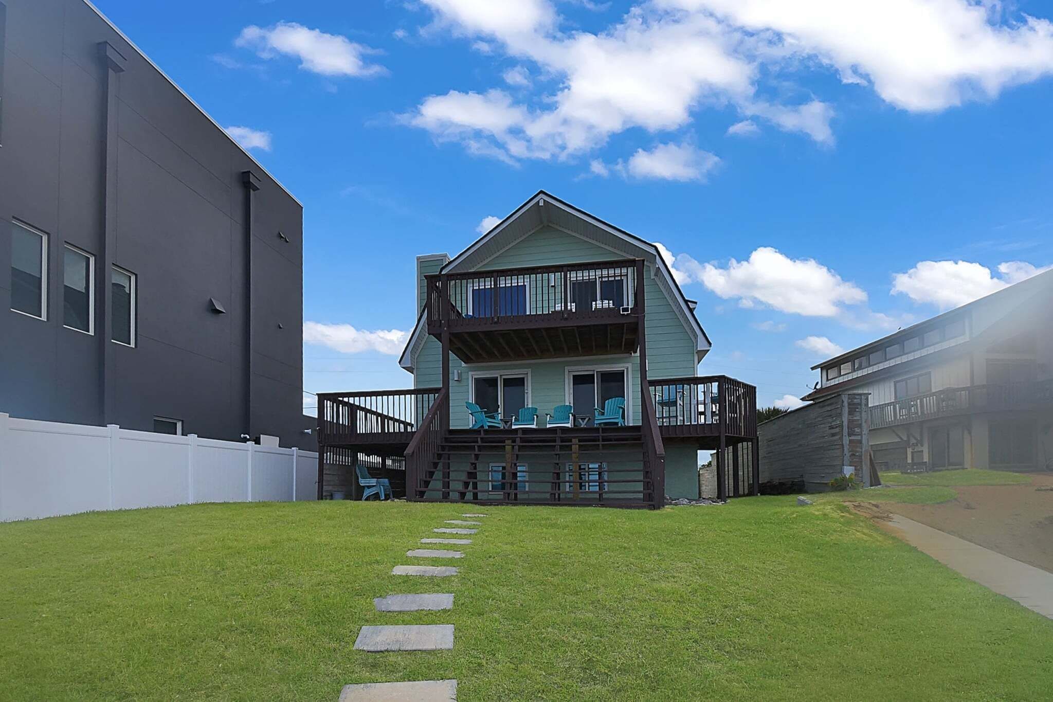 A two-story house with a balcony, a white fence, and a stone pathway leading to the entrance.