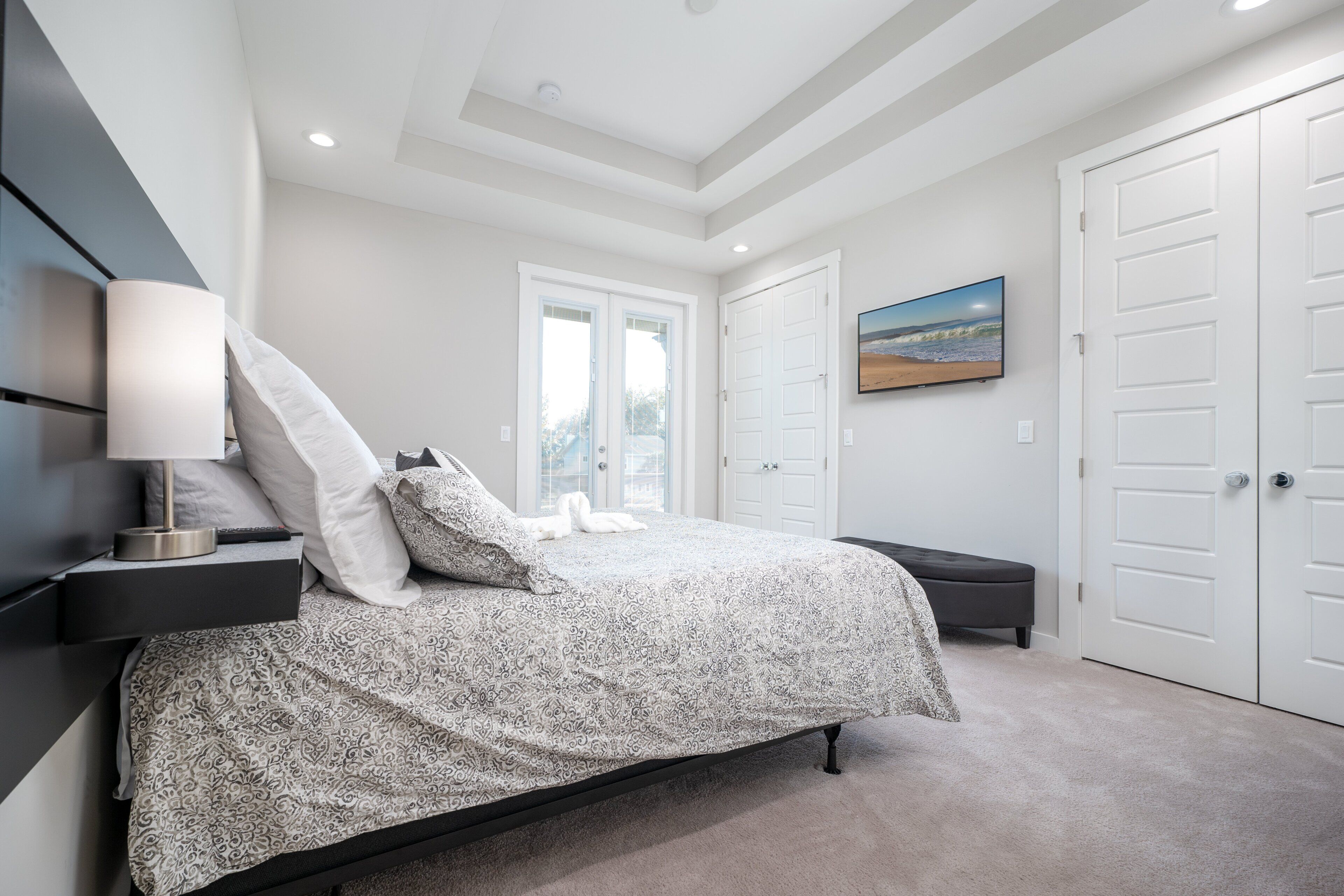 A bedroom with a bed, nightstands, a lamp, a bench, a painting, and double doors.