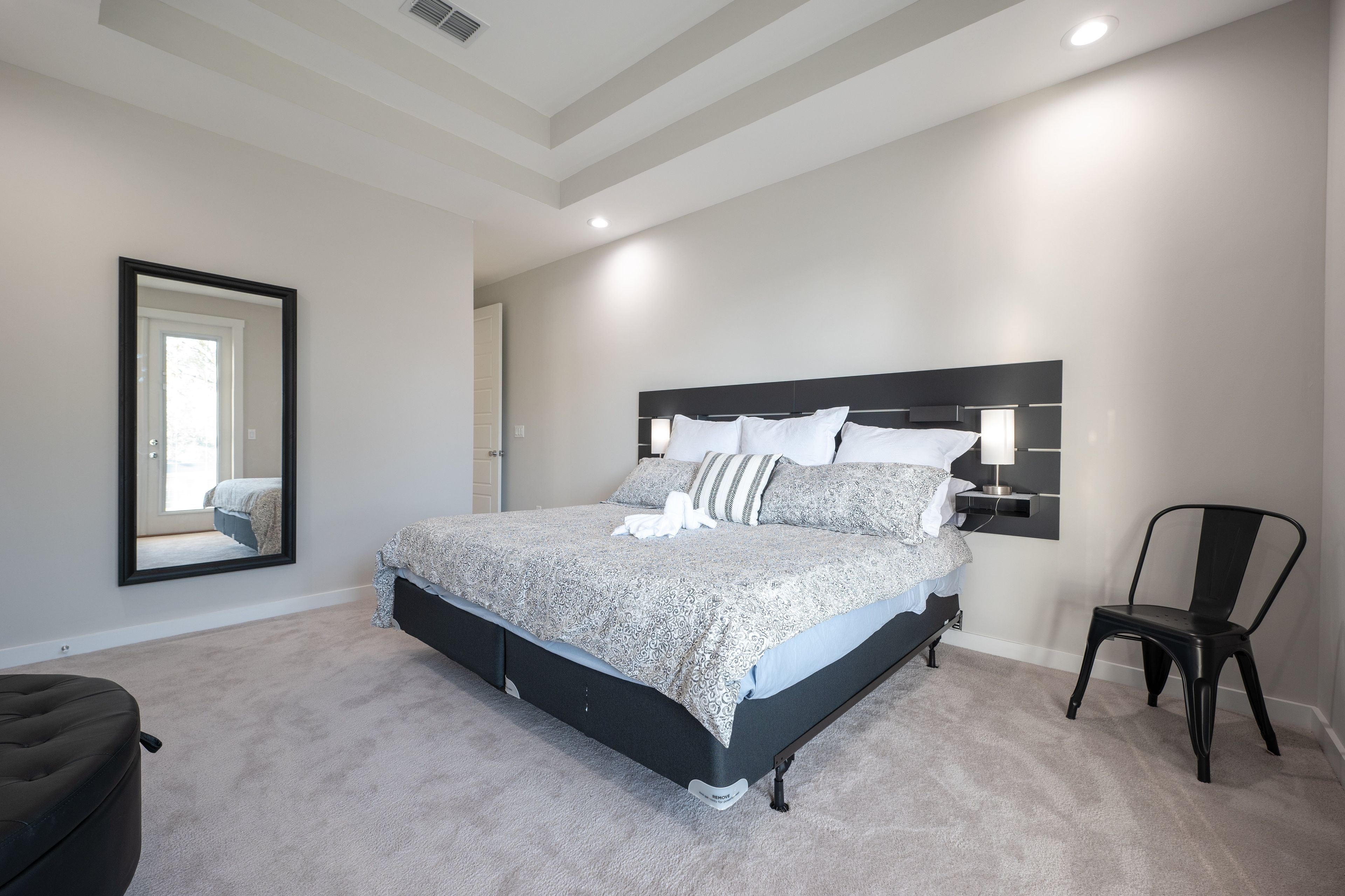 A bedroom with a large bed, a chair, a mirror, and a nightstand.