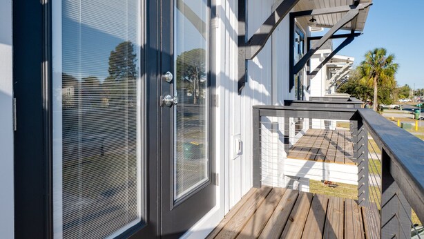 A wooden deck with a sliding glass door, a railing, and a clear blue sky in the background. - Pet-friendly 4BR Beach Home Walk to Beach & Jacksonville Beach Pier Fenced Yard (Jacksonville Beach)
