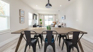 A dining area with a long table, six chairs, a hanging light fixture, and framed artwork on the walls. - Pet-friendly 4BR Beach Home Walk to Beach & Jacksonville Beach Pier Fenced Yard (Jacksonville Beach)