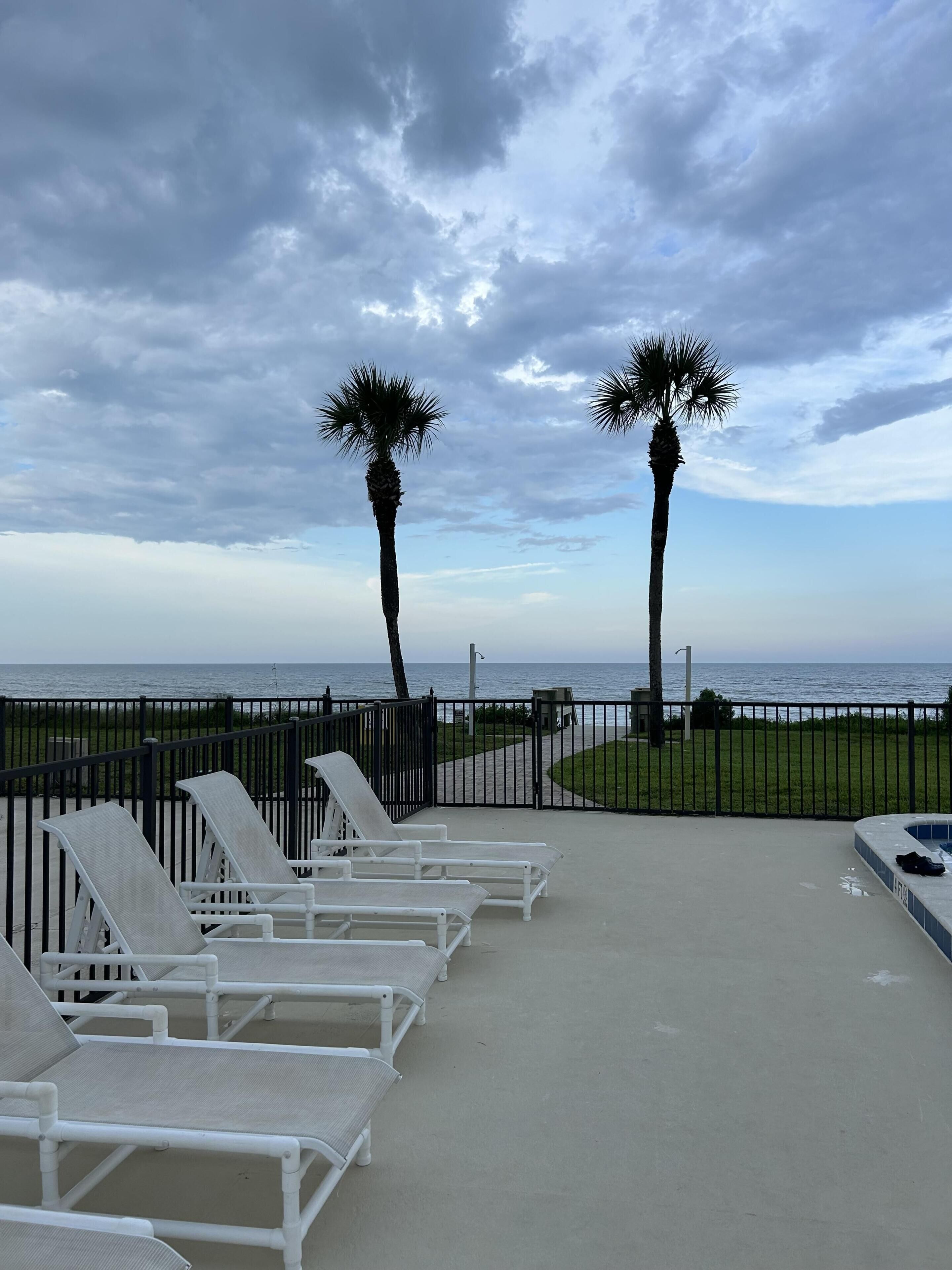 Un salón junto a la playa con sillones blancos, palmeras y vista al océano.