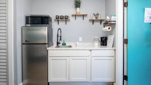 Una cucina compatta con frigorifero in acciaio inossidabile, forno a microonde, lavello con rubinetto e un piano di lavoro con diversi oggetti.