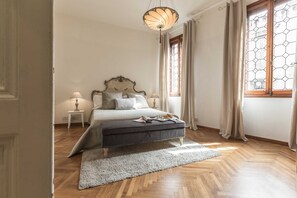 Ein Schlafzimmer mit einem Bett, Nachttischlampen, einem Teppich und einem Fenster mit Vorhängen.