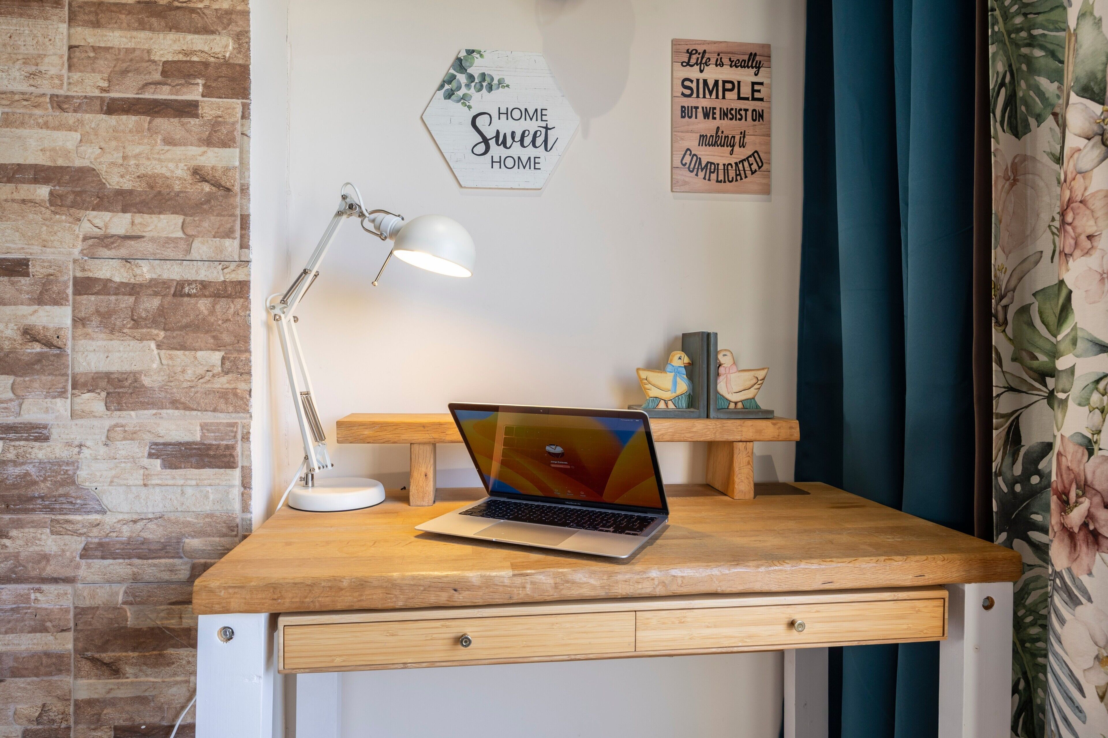 A wooden desk with a laptop, a desk lamp, and a small shelf with figurines.