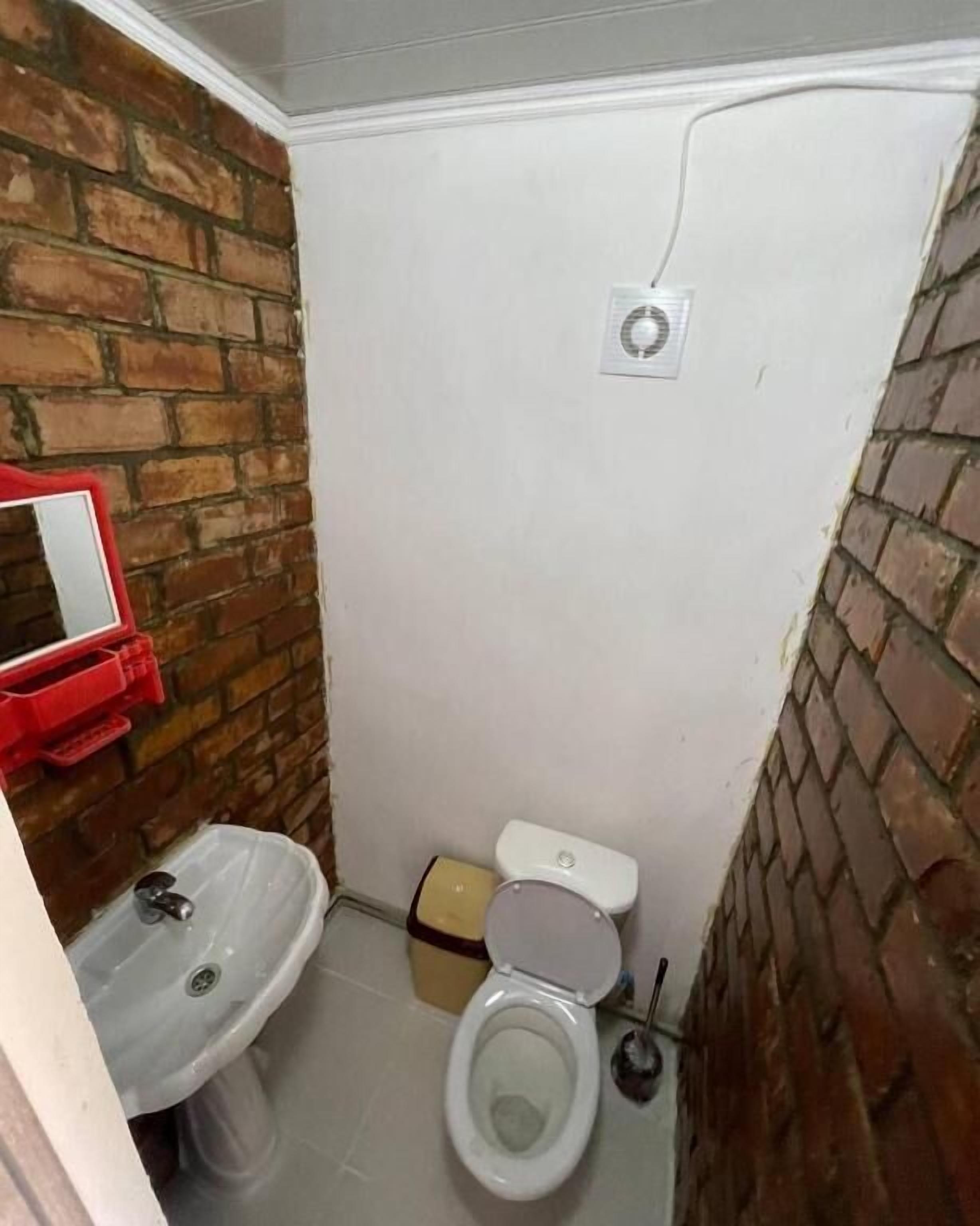 A small bathroom with a white sink, toilet, and a red-framed mirror.
