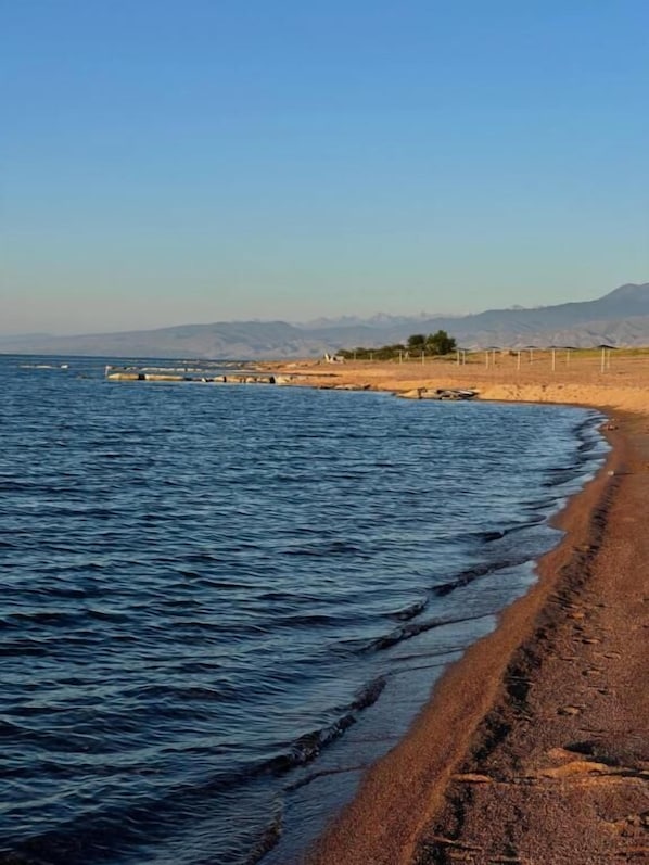 A beach with a clear sky, calm water, and distant mountains.