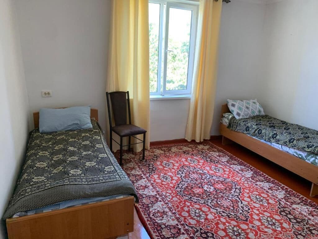 Una habitación con dos camas individuales, una silla, una ventana con cortinas y una alfombra estampada.