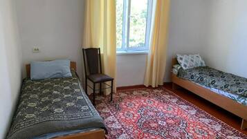 Una habitación con dos camas individuales, una silla, una ventana con cortinas y una alfombra estampada.