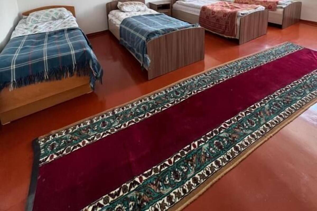 A room with three beds, a large red rug, and a painting on the wall.