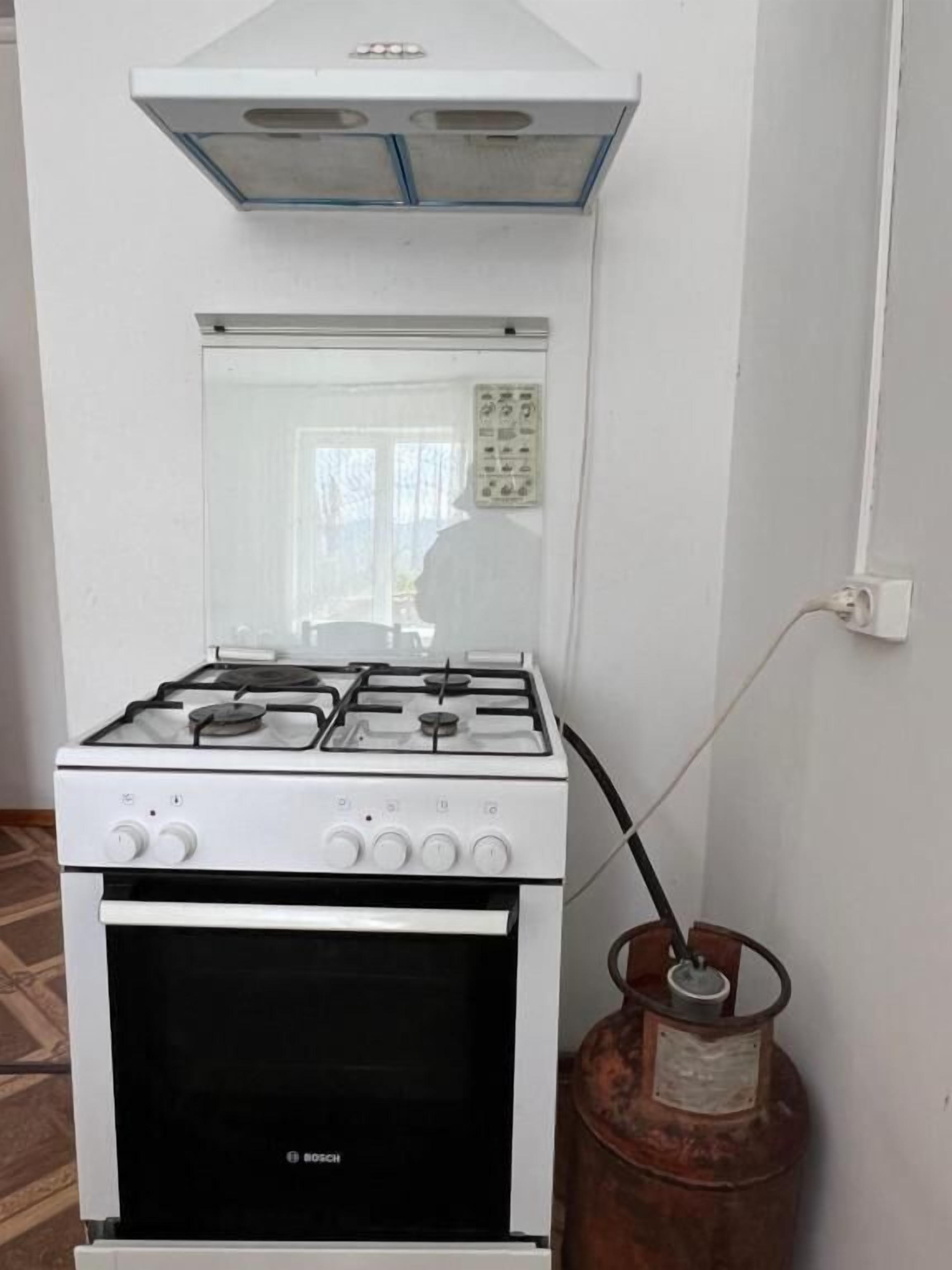 Une cuisinière à gaz blanche de la marque Bosch, dotée de quatre brûleurs, d’une hotte aspirante et d’un four situé en dessous.