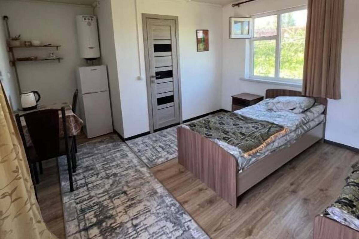 A compact room with a bed, a small desk, a chair, a radiator, and a window.