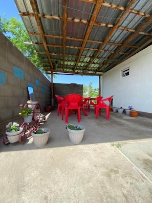 A covered outdoor area with a concrete floor, red plastic chairs, and potted plants.