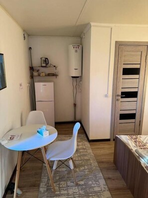 A compact room with a small table, two chairs, a refrigerator, a water heater, and a wooden door.
