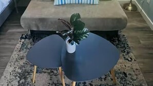 Een moderne woonkamer met een bank, een bijzettafeltje, een lamp en een raam met gordijnen.