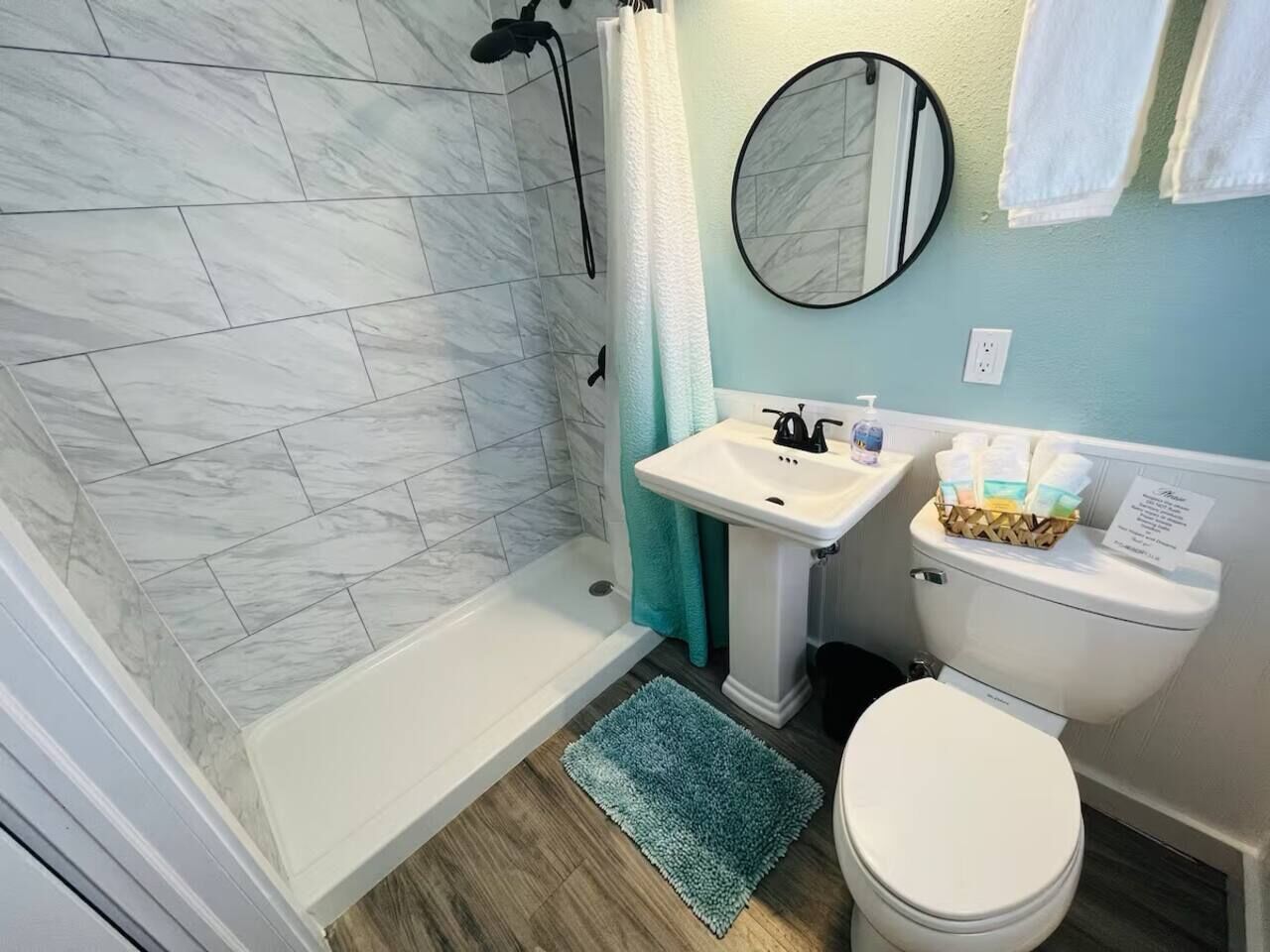 A bathroom with a shower, sink, toilet, and a mirror.