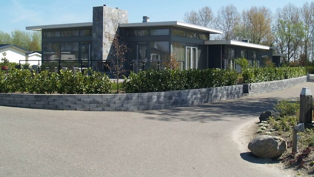 Una casa moderna de dos pisos con fachada de piedra, ventanas grandes y un jardín delantero ajardinado.