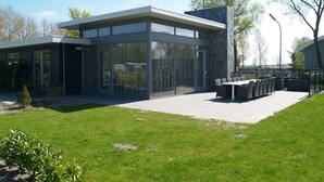Un edificio moderno con amplios ventanales, techo plano y un patio con mobiliario exterior.