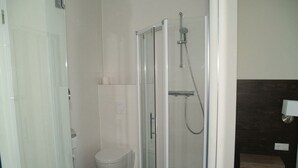 Un baño con cabina de ducha de vidrio, inodoro y tocador de madera oscura.