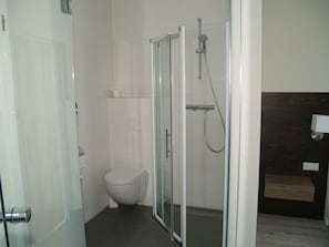 Ein Badezimmer mit Duschkabine aus Glas, Toilette und dunklem Holzwaschtisch.