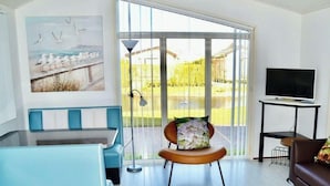 Una sala de estar moderna con un sofá, un sillón con un cojín floral, un televisor sobre un mueble bajo y un cuadro con gaviotas en la pared.