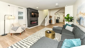 A modern living room with a fireplace, a sofa, a coffee table, and a staircase leading to another room.