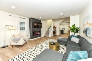 Ein modernes Wohnzimmer mit Kamin, einer Couch, einem Couchtisch und einer Treppe, die in einen anderen Raum führt.