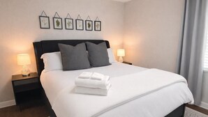 Un llit ben arrugat amb llençols blancs i almoines grises, dues làmpades de nit i gravats botànics emmarcades a la paret.