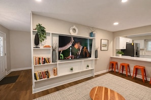 A living room with a flat-screen TV, bookshelves, a coffee table, and orange stools. - 4BD 2BA Ranch on Catherine Westfield Fenced Yard (Westfield)