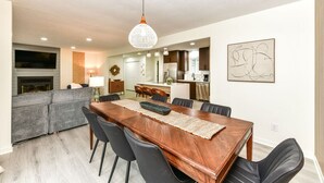 Uma cozinha moderna com armários escuros, uma ilha central e um espaço de jantar com mesa e cadeiras de madeira.