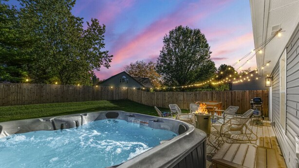 Een hottub met een houten terras, buitenmeubels en sfeerverlichting.