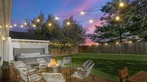 Un jardin avec une terrasse, des meubles d’extérieur, un barbecue et des guirlandes lumineuses.