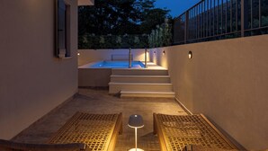 Un espace détente avec un jacuzzi, des marches menant à celui-ci et deux fauteuils de relaxation en osier.