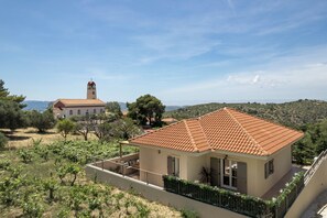 Une villa avec un toit en tuiles, un balcon et un vignoble en arrière-plan.