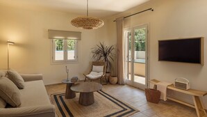 Un salon avec un canapé, une table basse ronde, un fauteuil, un téléviseur et une grande fenêtre.