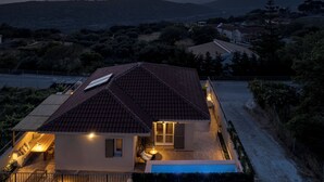 Une maison avec un toit en tuiles, une piscine et un patio aménagé avec du mobilier d’extérieur.