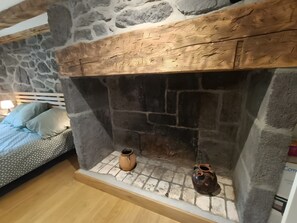 A stone fireplace with two vases, a bed with patterned bedding, and a lamp on a nightstand. - Holiday Home “Gîte 9 Personnes Puy Mary” with Mountain View, Private Terrace and Garden (Le Claux)
