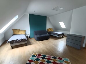 A room with a sloped ceiling, two beds, a sofa, a dresser, and a colorful rug. - Holiday Home “Gîte 9 Personnes Puy Mary” with Mountain View, Private Terrace & Garden (Le Claux)