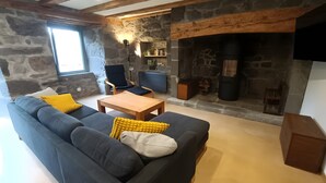A cozy living room with a stone fireplace, a dark sofa with yellow cushions, a wooden coffee table, and a stone wall.