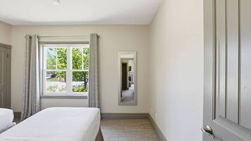 A hotel room with a bed, a window with curtains, a mirror, and a door.