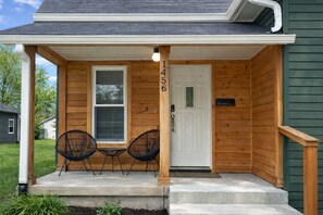 A wooden house with a porch, two chairs, a door, and a mailbox. - Grant’s Fresh Modern Charm 3B 2B (Noblesville)