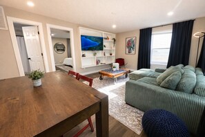 A living room with a wooden dining table, a sofa, a coffee table, and a TV. - Grant’s Fresh Modern Charm 3B 2B (Noblesville)