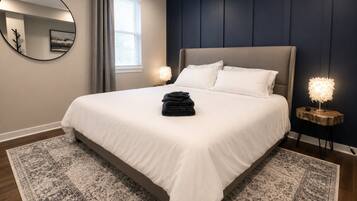 Un dormitorio con cama, espejo redondo, mesita de noche y ventana con cortinas.