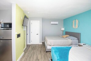 A hotel room with a bed, a nightstand, a lamp, a microwave, and a refrigerator. - 1915 Beach Club - Sunset Suite 7 (Daytona Beach)